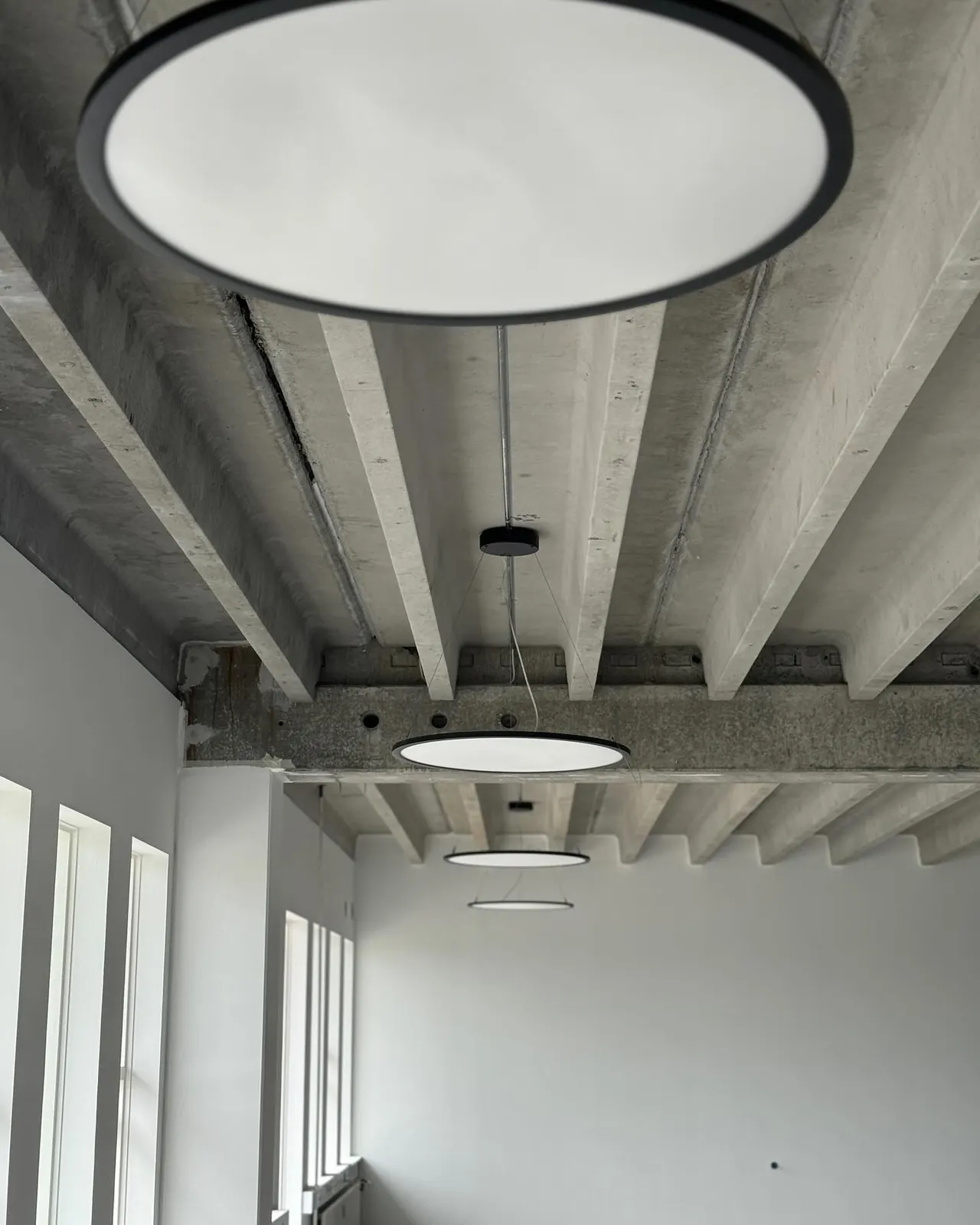 Runde lamper ophængt under et betonloft med synlige bjælker