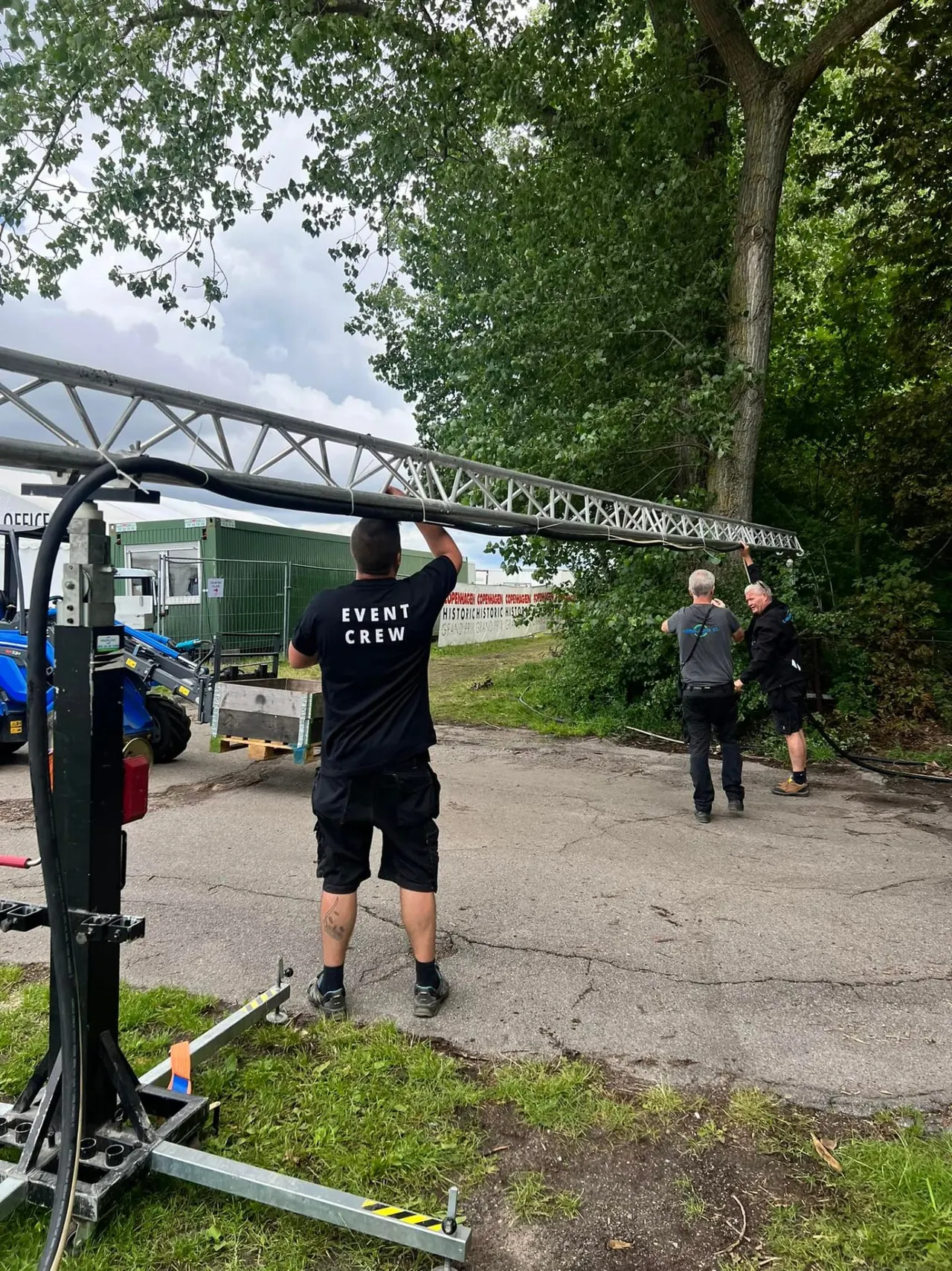 Eventcrew arbejder med truss og strømkabler bag scenen