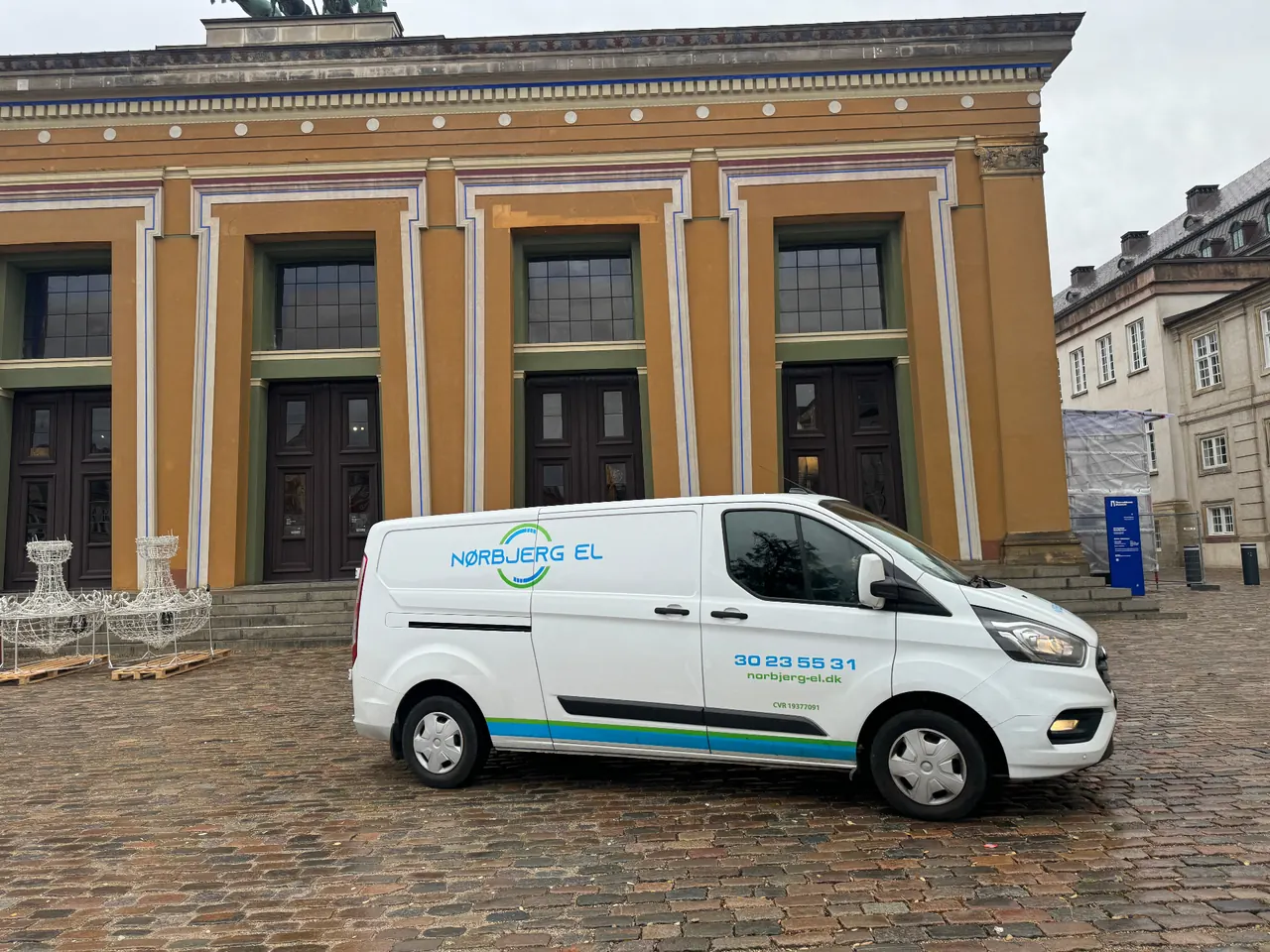 Hvid Nørbjerg El-varevogn parkeret på en brostensbelagt plads