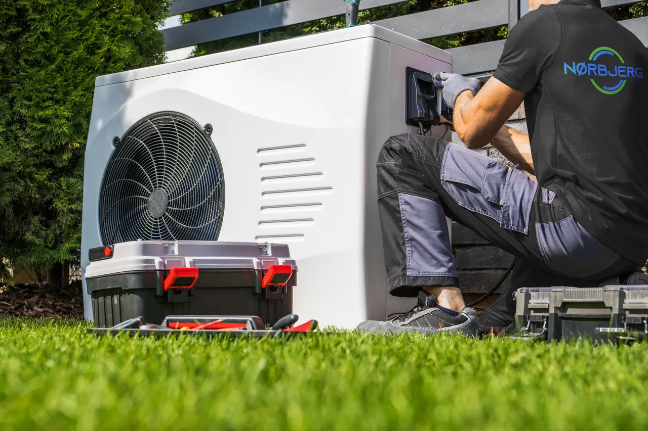 Montør arbejder med tilslutning af en varmepumpe udenfor et hus